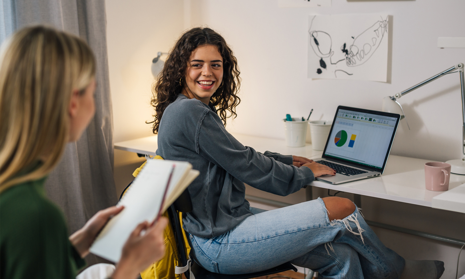 Two smiling women study in a dorm room